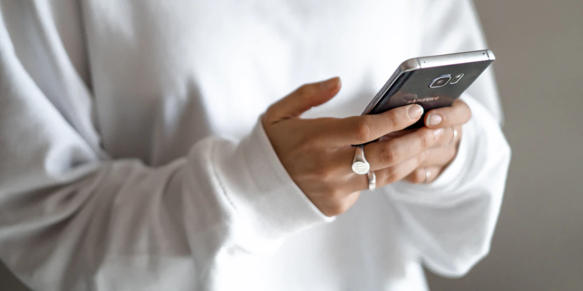 Persona con maglia bianca tiene in mano uno smartphone nero