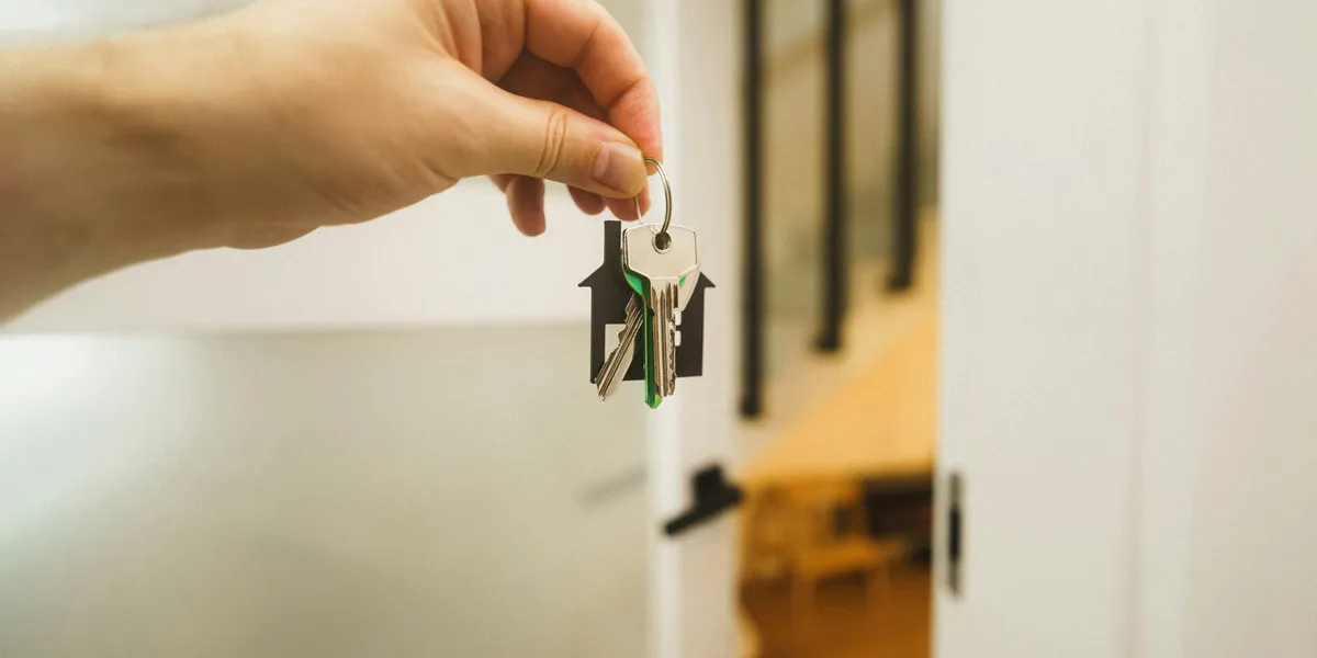 Mano che tiene un mazzo di chiavi con portachiavi a forma di casa davanti a una porta d'ingresso aperta