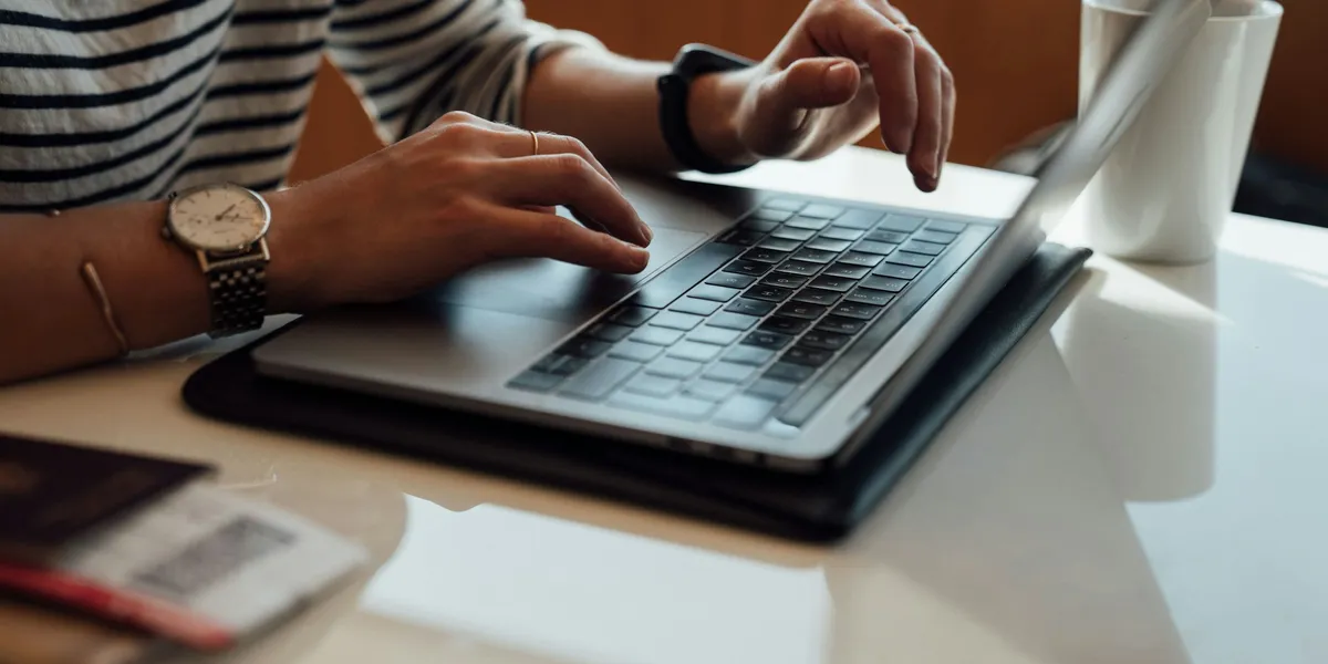 Mani digitano su un laptop aperto su un tavolo, accanto a una tazza bianca